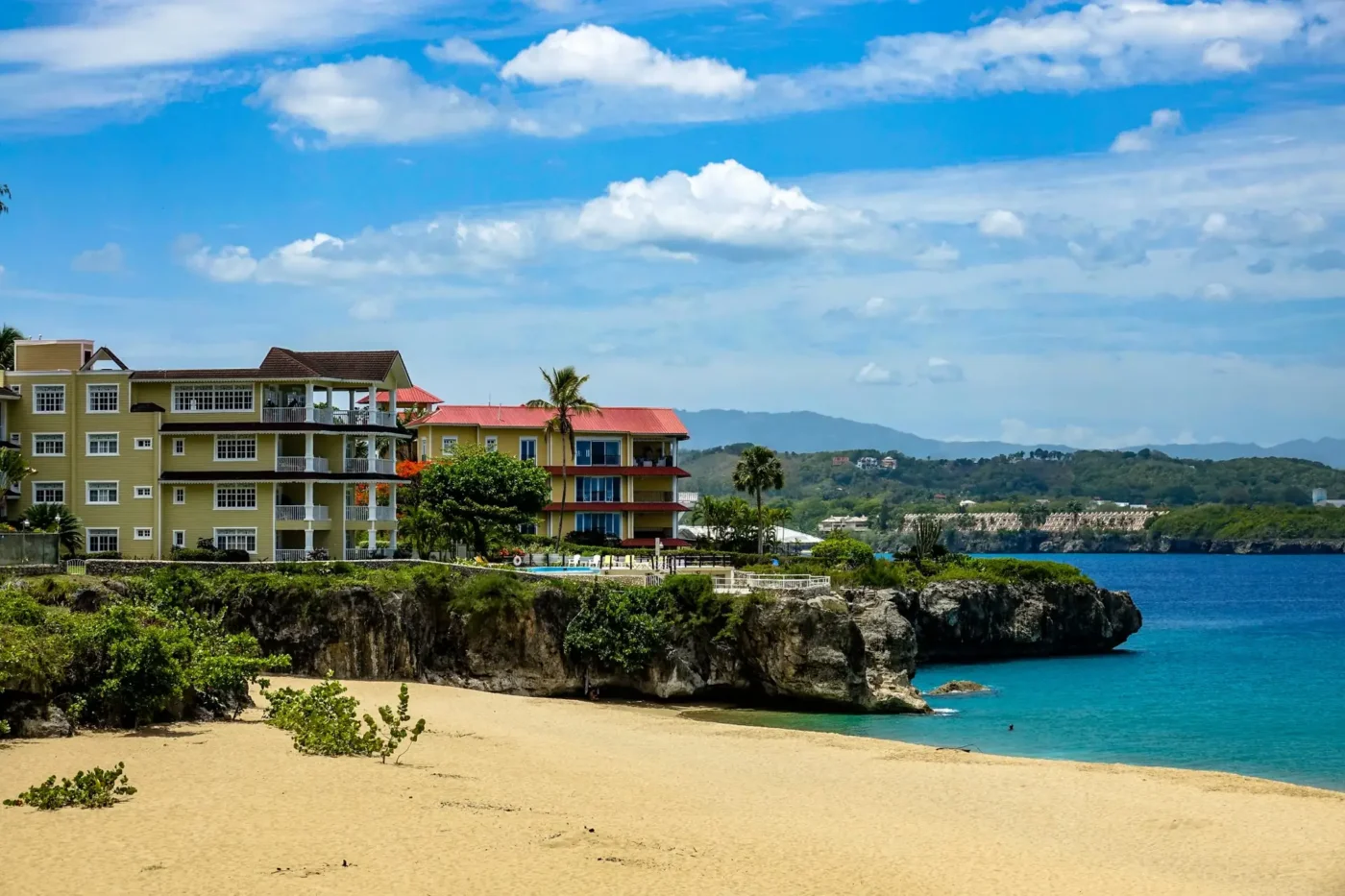 Low-rise coastal residences above a sandy beach and turquoise water