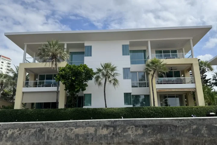 Three-storey white residence with wide balconies and palm-lined lawn
