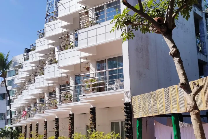 White apartment building with stacked balconies and greenery